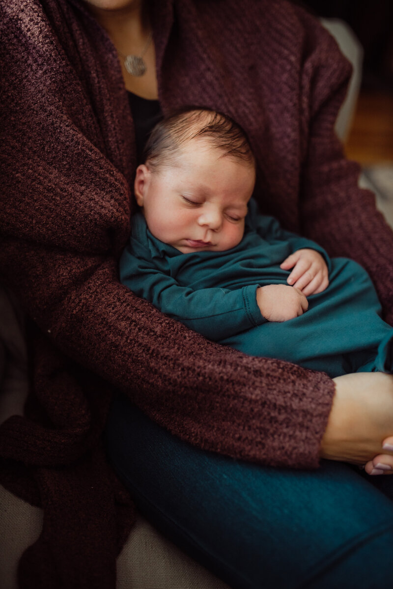 newborn baby swaddled in a blue blanket laying on womon's lap