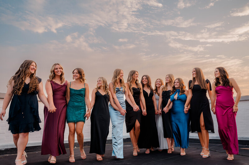 Rachel B Photography's Senior Rep Team of 14 seniors walk hand in hand in an open field  while smiling at one another.