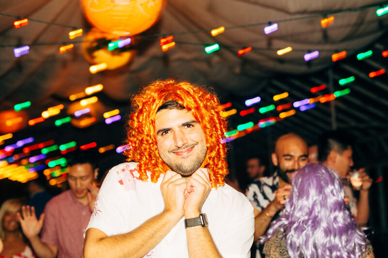A wedding guest wearing a brightly colored wig during the wedding reception at Dos Pueblos Orchid Farm, a wedding venue in Santa Barbara along the California coast.