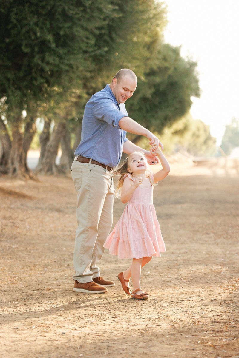 Daddy daughter dancing among the olive trees in a portrait session with Fresno Photographer One Good Shot Photography