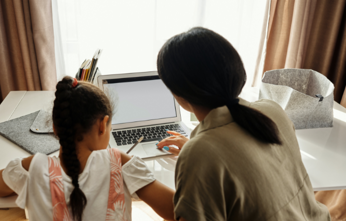 A woman and girl sitting at a laptop together, seen from behind