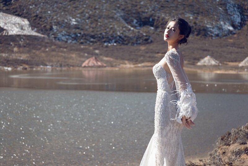 Dramatic shoot of a bride in a haute couture dress by an alpine lake in snow capped mountains.