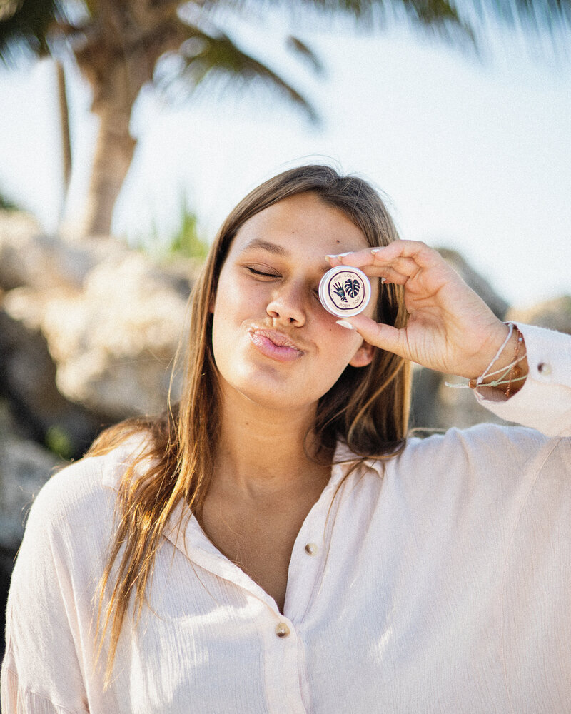 Model poses with natural lip balm on beach for product photoshoot