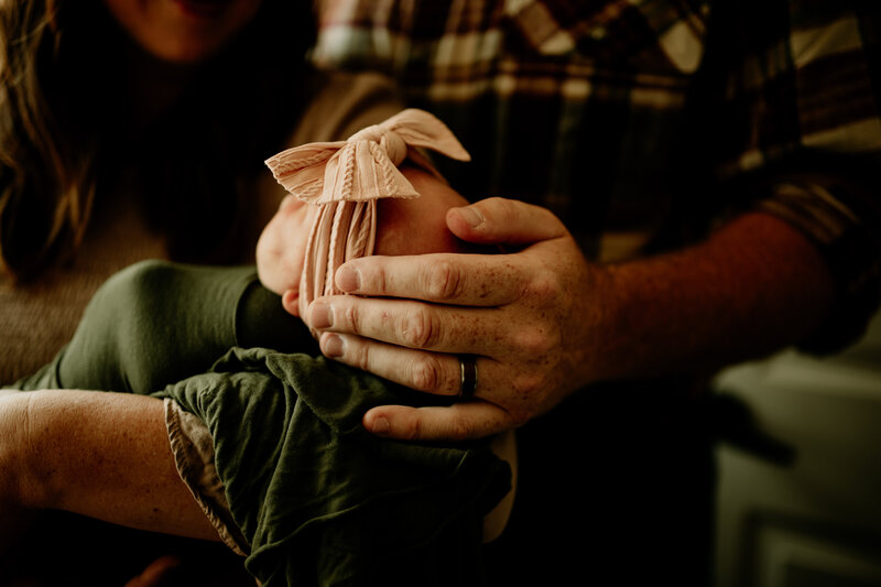 A dad gently caresses his newborn daughter's head during an in-home family session.