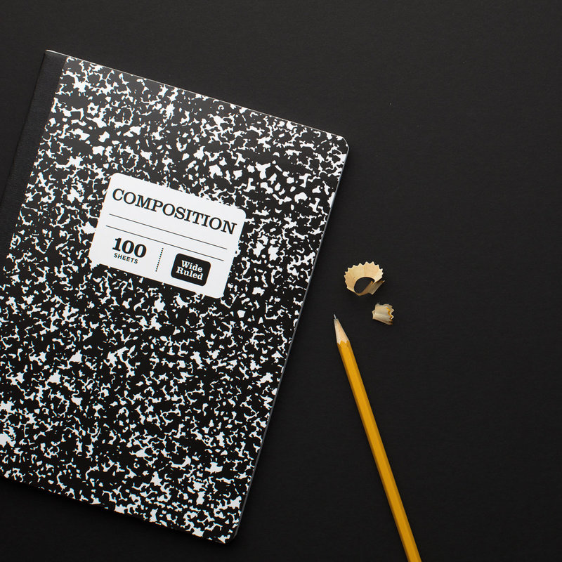 composition notebook on a black background with a yellow number two pencil and pencil shavings.
