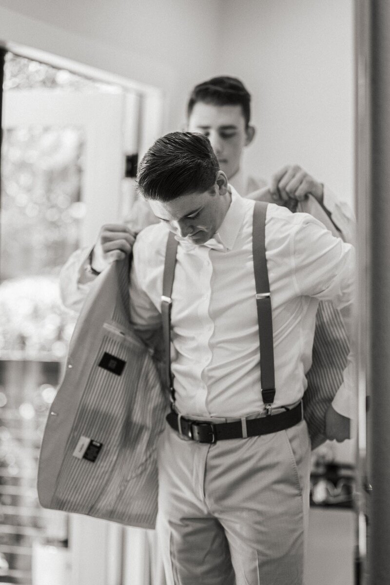 Photo of groomsman helping groom into jacket. Black and white