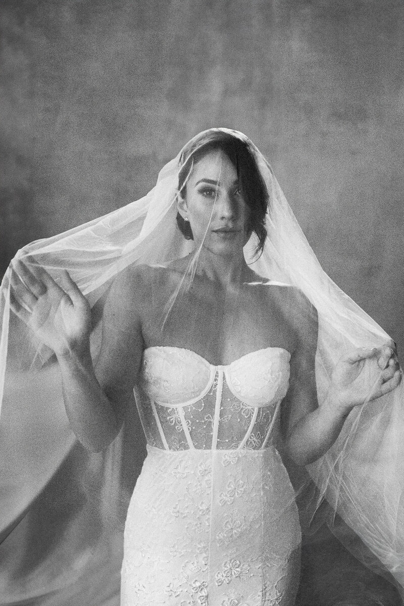 Black and white photo of bride holding her veil over her face with her hand in front of her