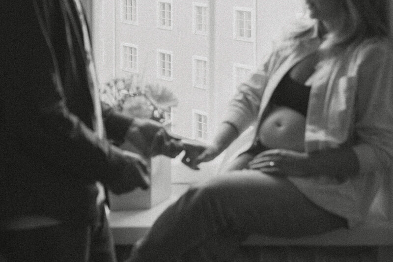 Pregnant woman sitting on the windowsill and holding her partners hand at their home in Helsinki