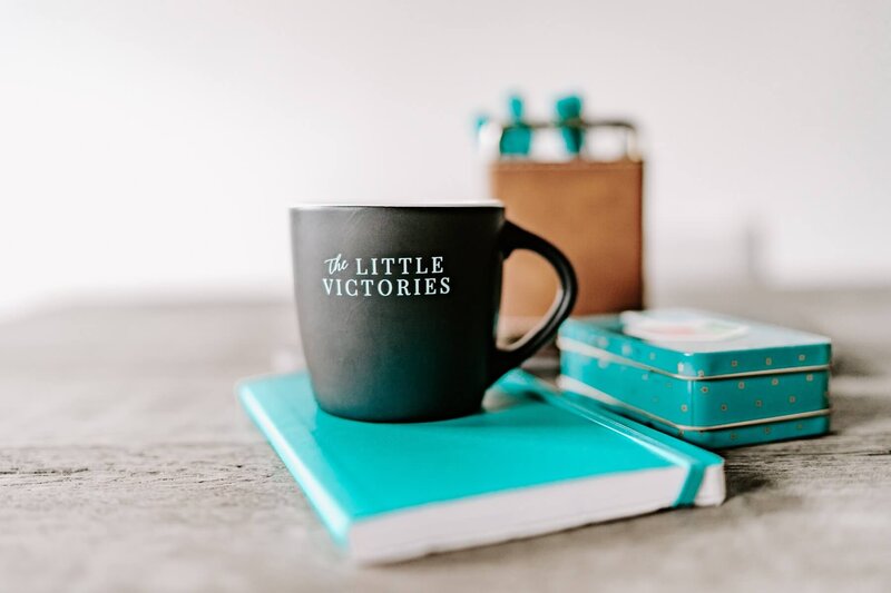a notebook with a mug sitting on top of it that says "The Little Victories"