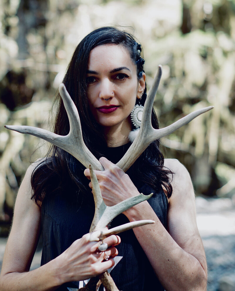 Founder of Alchemy Queen holding deer antlers in front of her heart. 