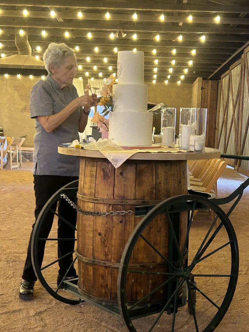 Artful Sweets pastry chef arranging sugar flowers on tiered wedding cake at barn venue