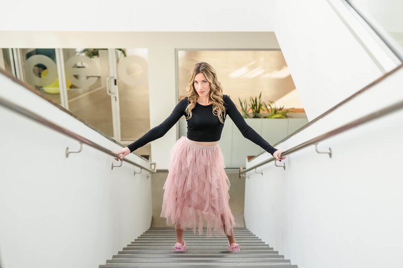 Renee Warren wearing pink skirt and standing in power pose on stairs of the Innovation Centre downtown Kelowna
