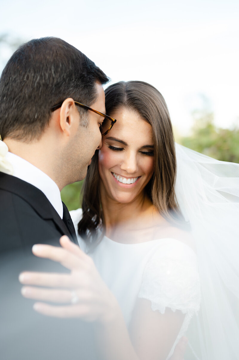 close up photo of wedding couple snuggling with veil swooped in front of them