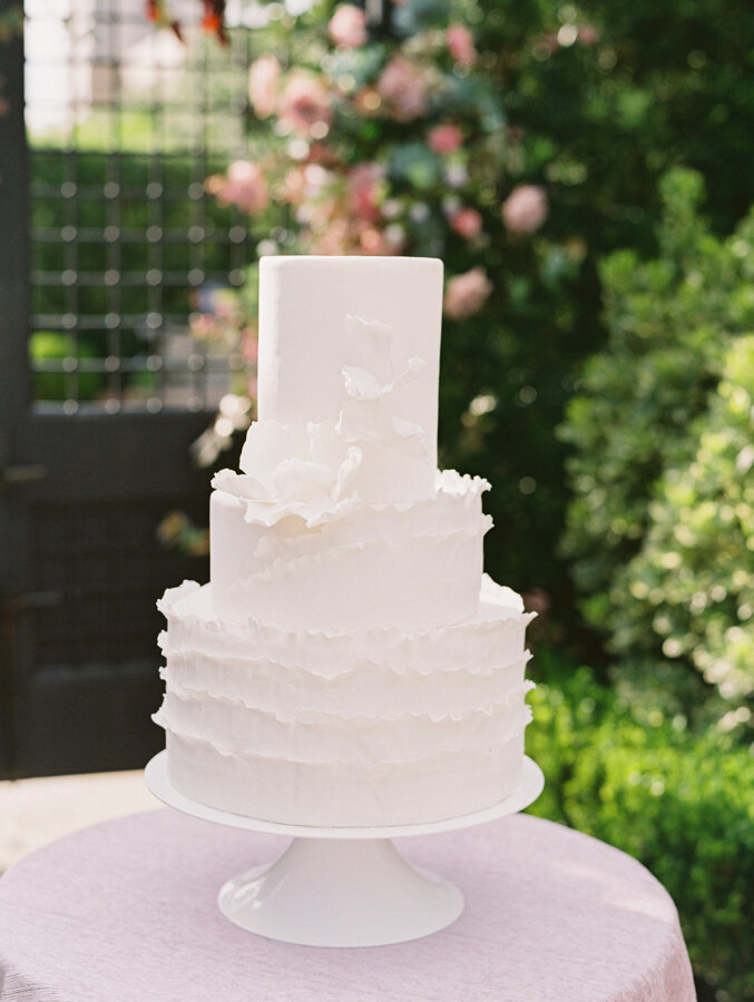 White tiered wedding cake sitting on a lavender tablecloth