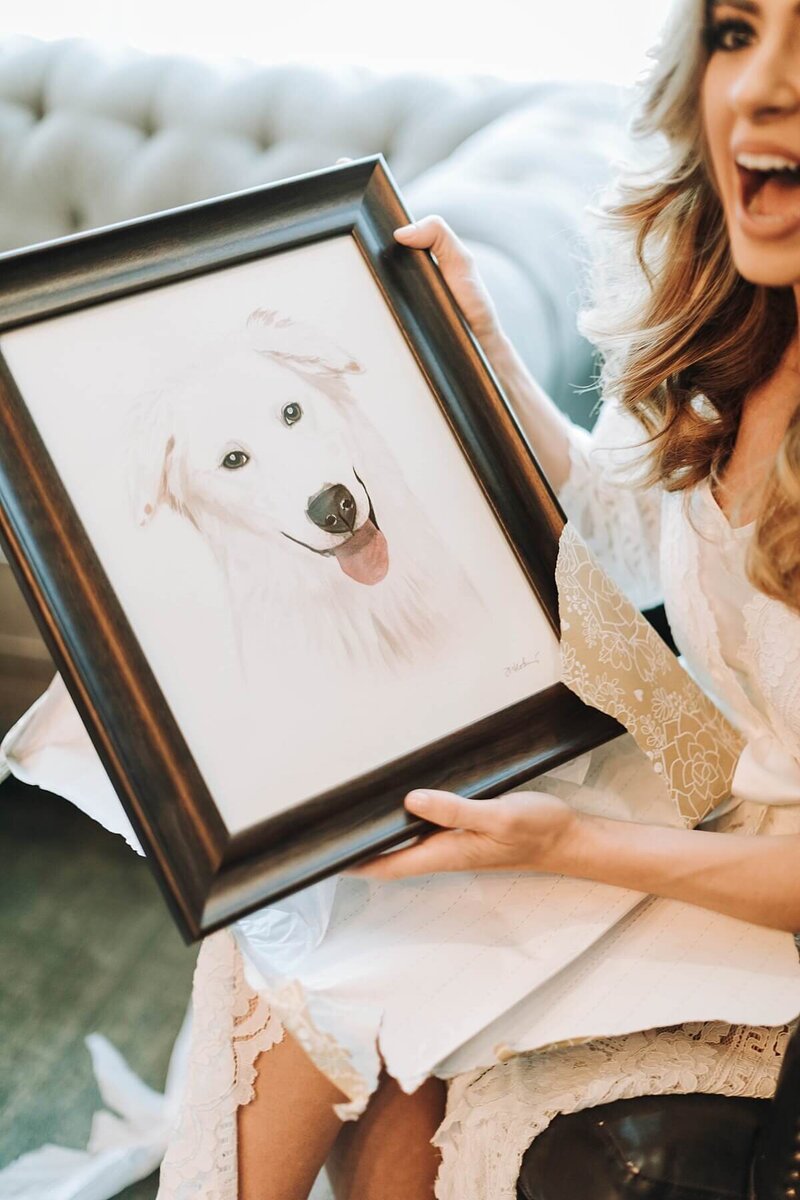 Bride smiling as she unwraps the gift from her groom a painted portrait of their dog