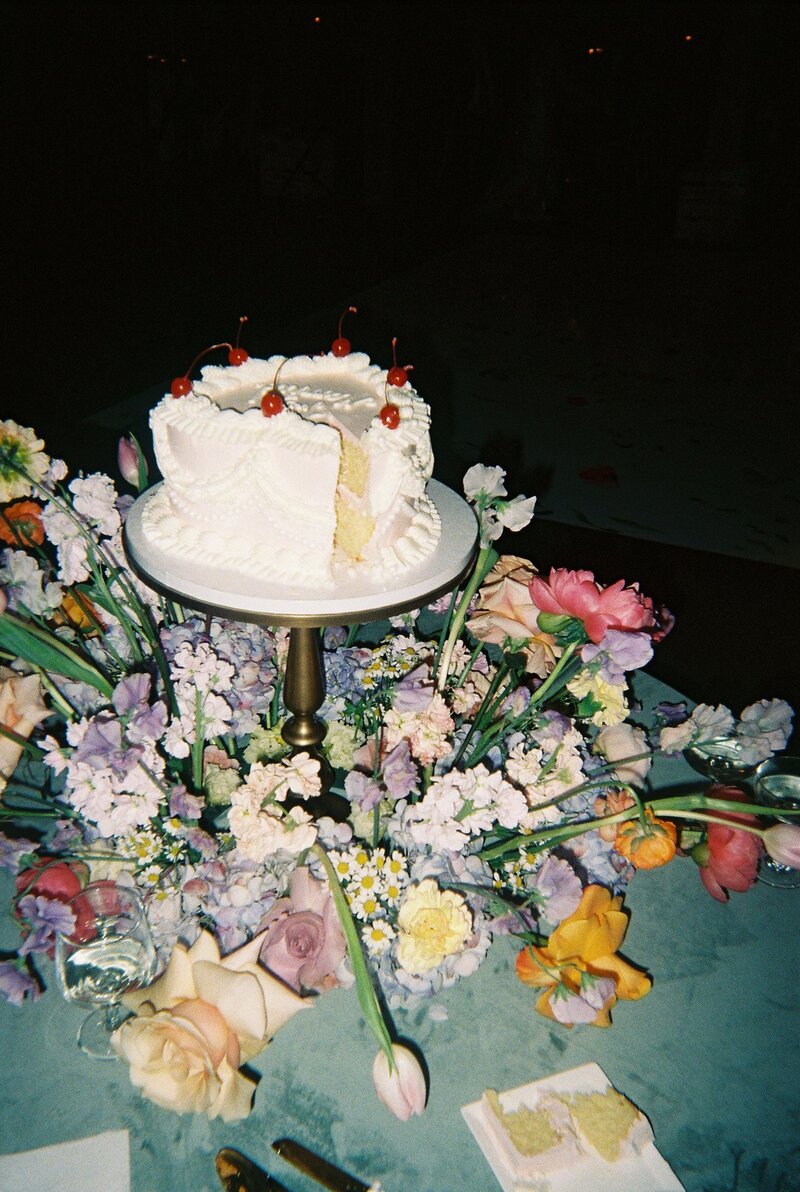 Flash film photo of wedding cake with slice cut out of it surrounded by flowers