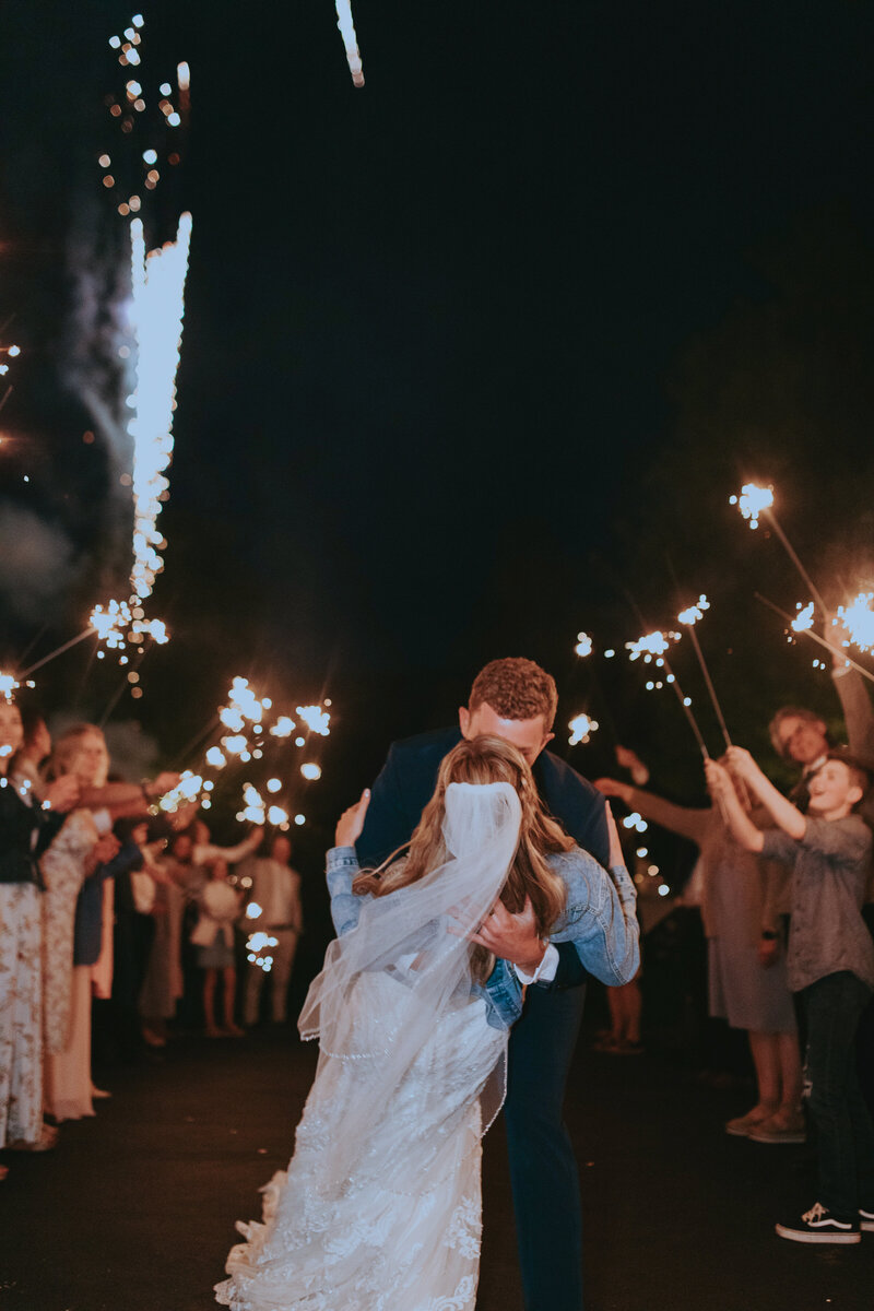 A couple share a PASSIONATE kiss among friends, sparklers and fireworks.