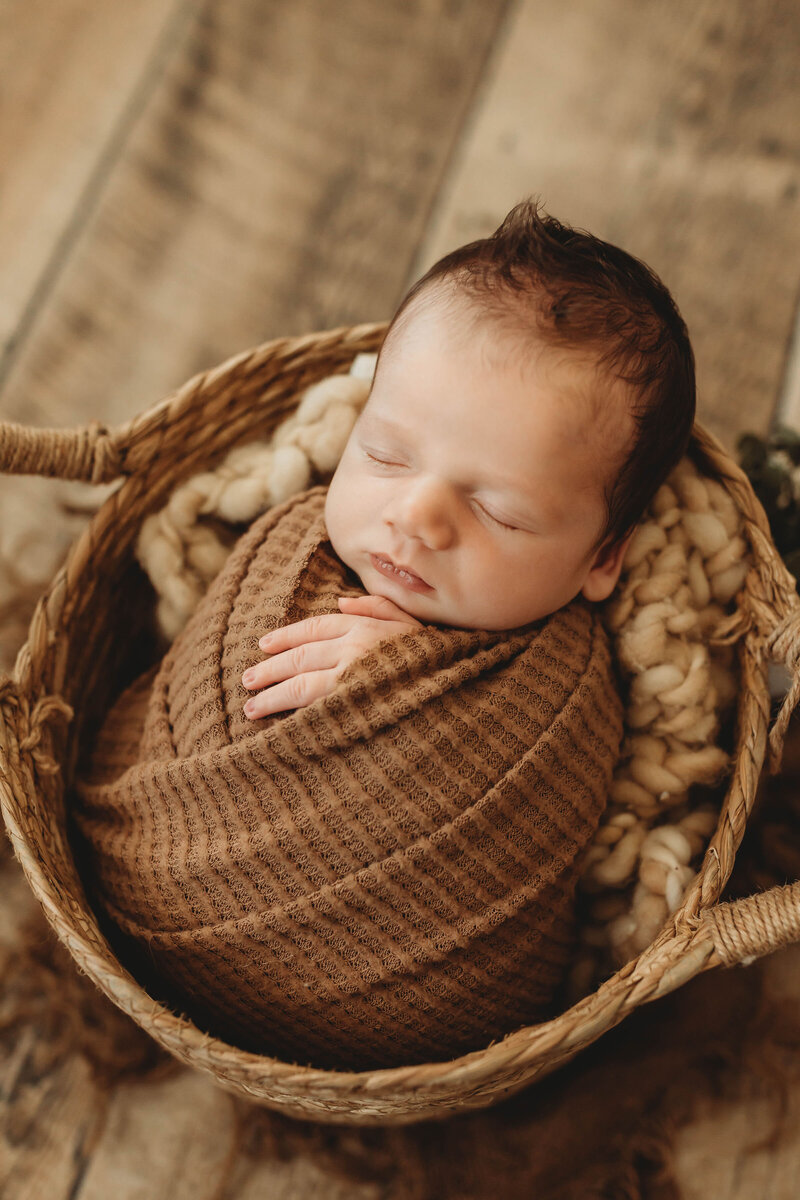 newborn wrapped in a brown blanket and in a basket
