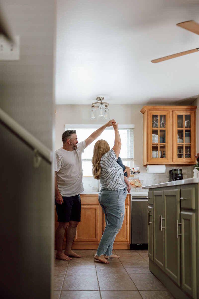 Couple dancing in their kitchen while holding their baby. 