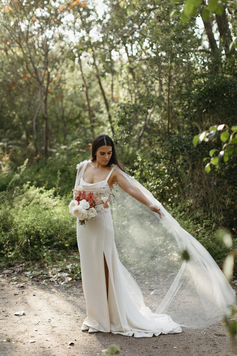 Bride tosses her wedding cape into the wind in dappled light during her wedding in Prince Edward County. Photographed by Jennifer van Son Photography in PEC