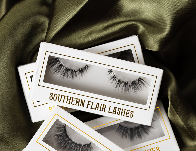 boxes of southern flair lashes on  green silk as a product photography piece by emmiclaire branding photographer in richmond, va