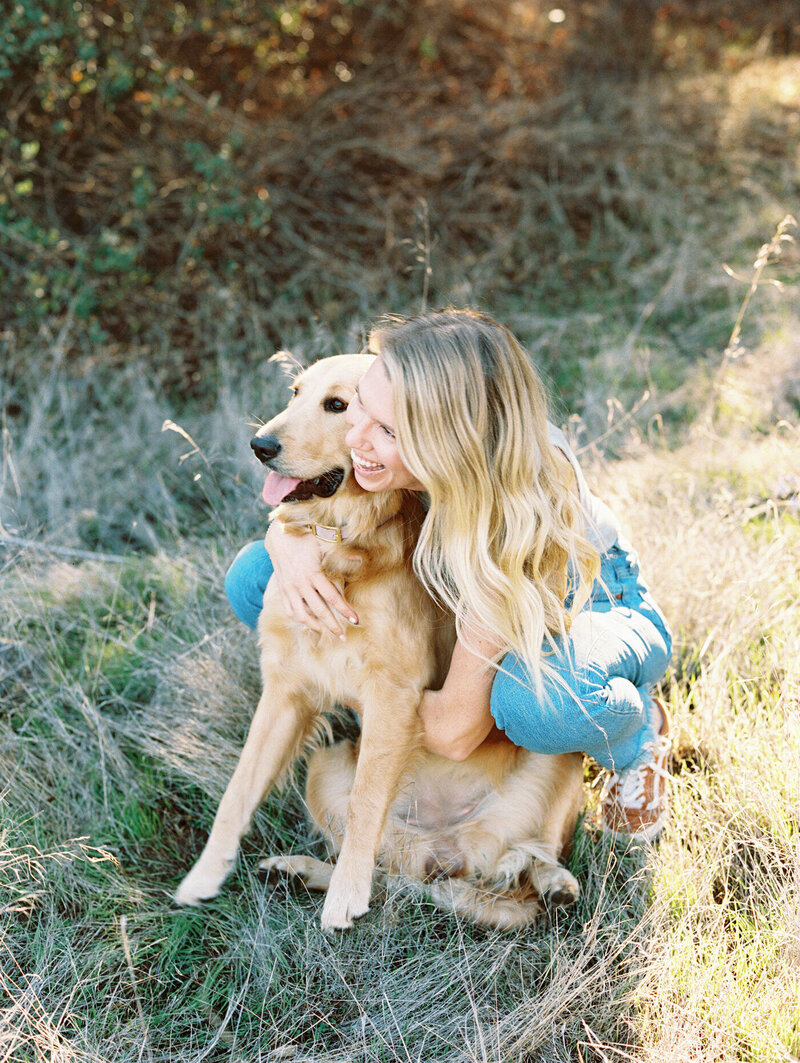 young woman wearing jeans holding on to her dog and smiling