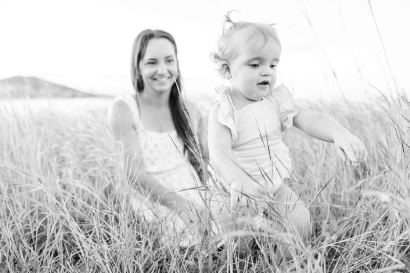 Black and white portrait taken by Yeppoon Family Photographer, of a mum with her little toddler girl who is inspecting a butterfly.