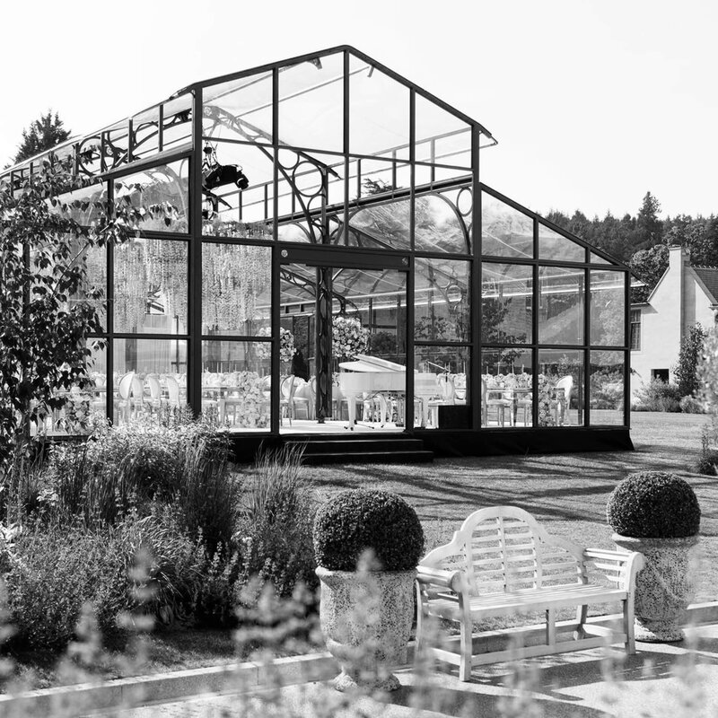 An aerial view of a glass marquee on a lawn with a long walkway and flowers at the entrance for Amelia and Olly Murs