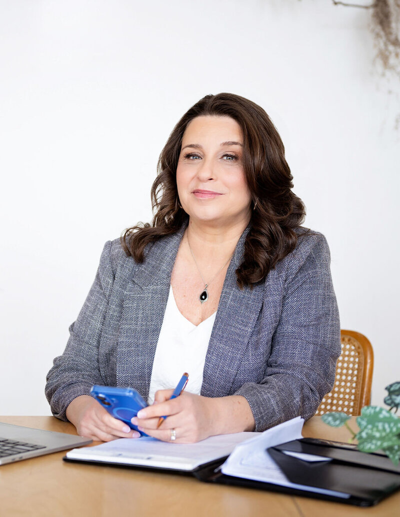 Dr. Chris Limone sitting at a desk with a notebook, pen, and phone, smiling confidently as a professional coach