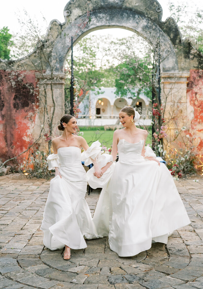 Stunning brides in wedding gowns hold hands and run joyfully on their wedding day