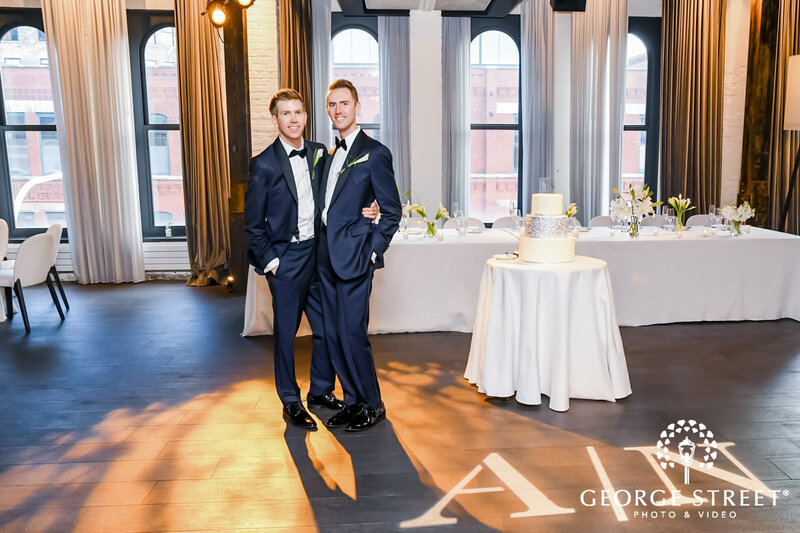 Grooms pose in front of wedding cake