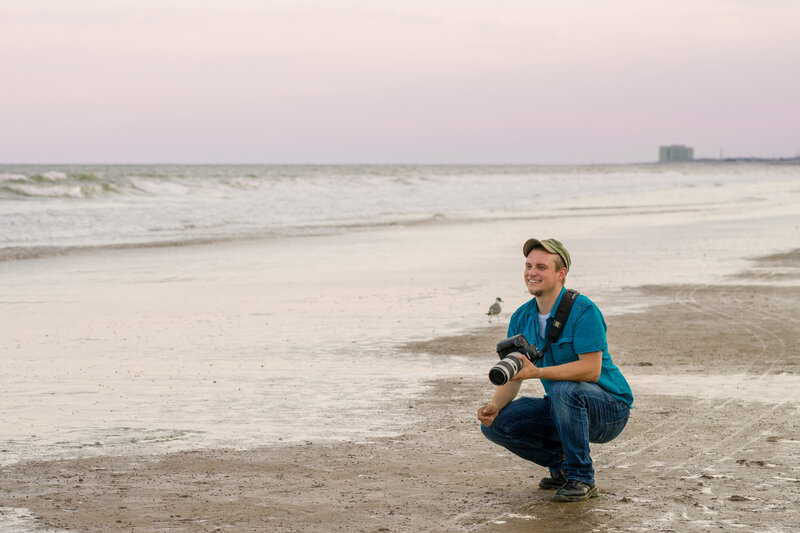 Travis Stitt holding a Canon camera on the beach at a New Jersey Shore engagement session, capturing stunning photos of the engaged couple in a picturesque coastal setting.