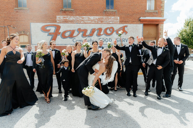 wedding party in sleek black attire poses joyfully against vintage mural, candid photography for modern romantic couples
