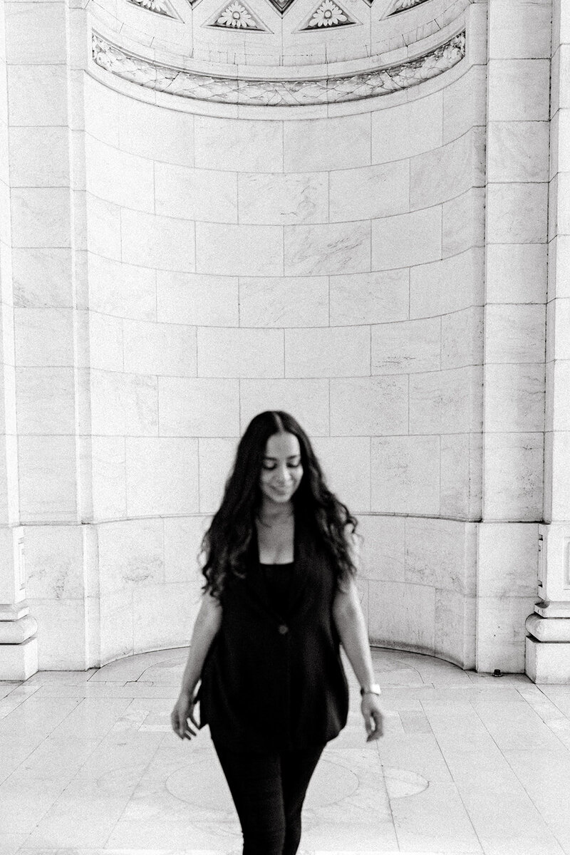 Florida wedding photographer, Melanie Anne, smiles in a black vest in front of the nee york city library