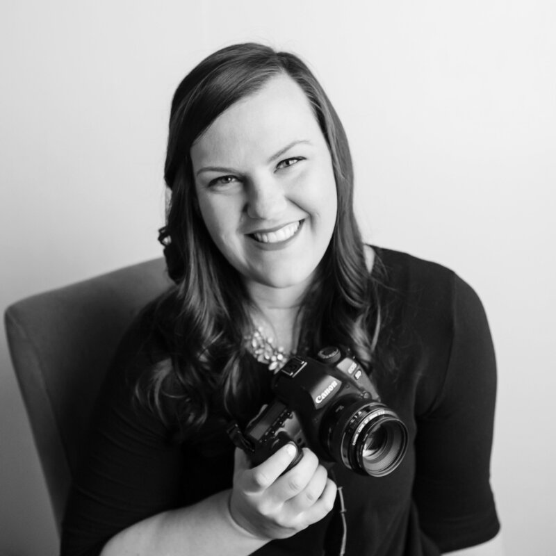 Black and white photo of wedding photographer in savannah, georgia names Brittany McCool. She is holding her Canon camera in one hand and wearing a black shirt and diamond necklace. Text reading "photographer, storyteller, mama x three overlays the image.