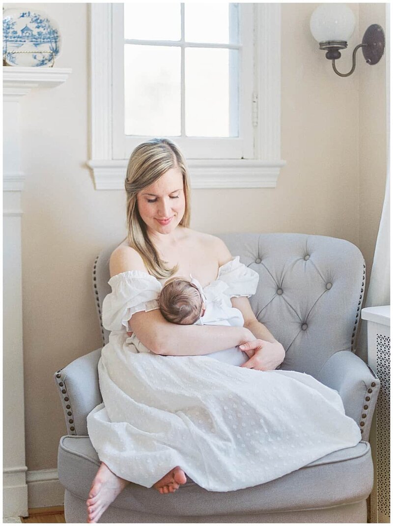 DC Family  Photographer holds her baby girl while sitting in a gray chair in her living room, smiling down at her baby