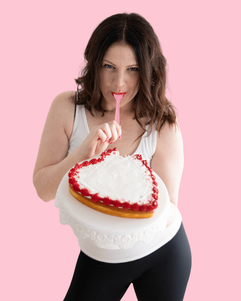 Emily, branding expert, holding a heart shaped cake in one hand and a fork in her mouth in the other.