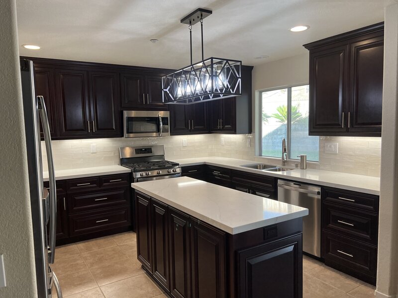 A new kitchen remodel with white countertops, a white backsplash and dark wood cabinets.