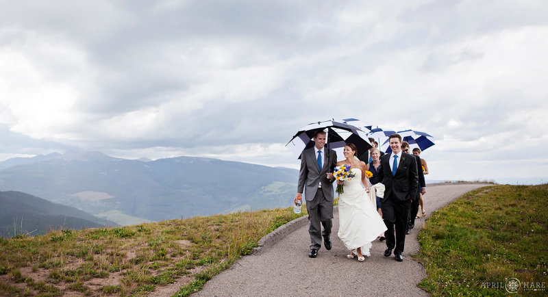 Wedding party walks under umbrellas at the Holy Cross Event Deck at Vail Resort Weddings in Colorado