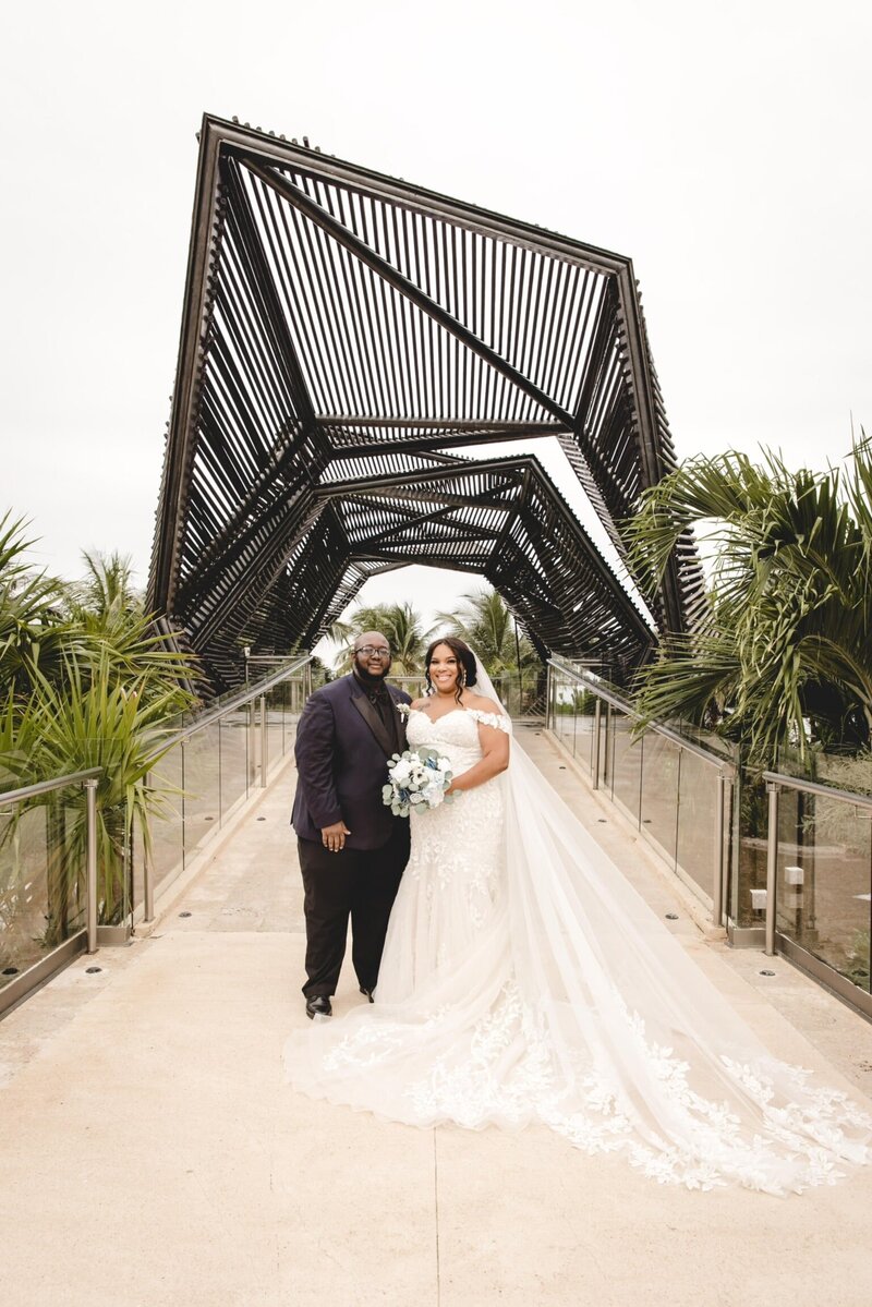 A bride and groom walking under a bridge.