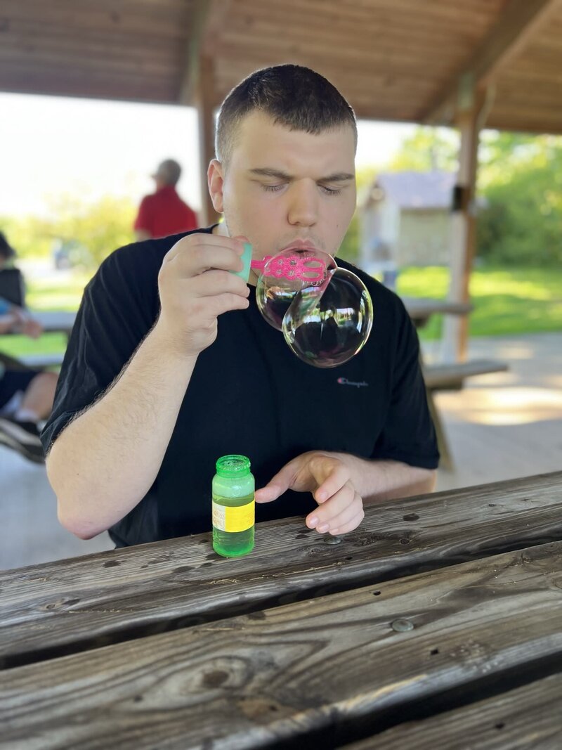 Image of solid rock friend blowing bubbles sitting on picnic table.