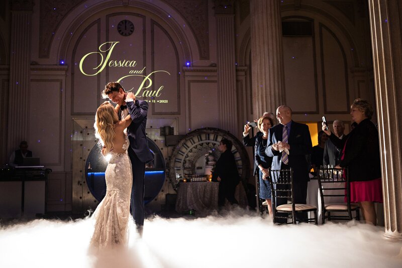 Bride and groom on a foggy dance floor with spectators on the right taking photos