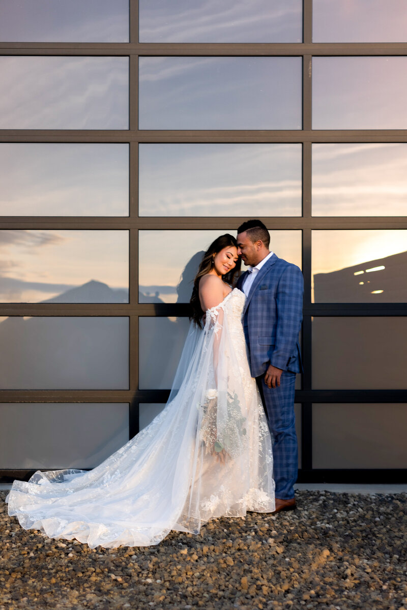Couple standing in front of the glass doors with a gorgeous sunset reflection in the glass.