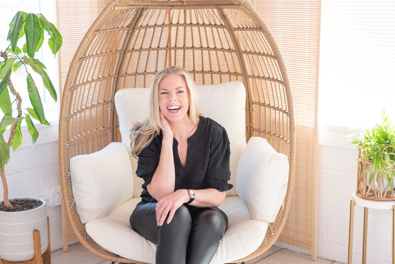A woman sitting in an egg chair laughing.