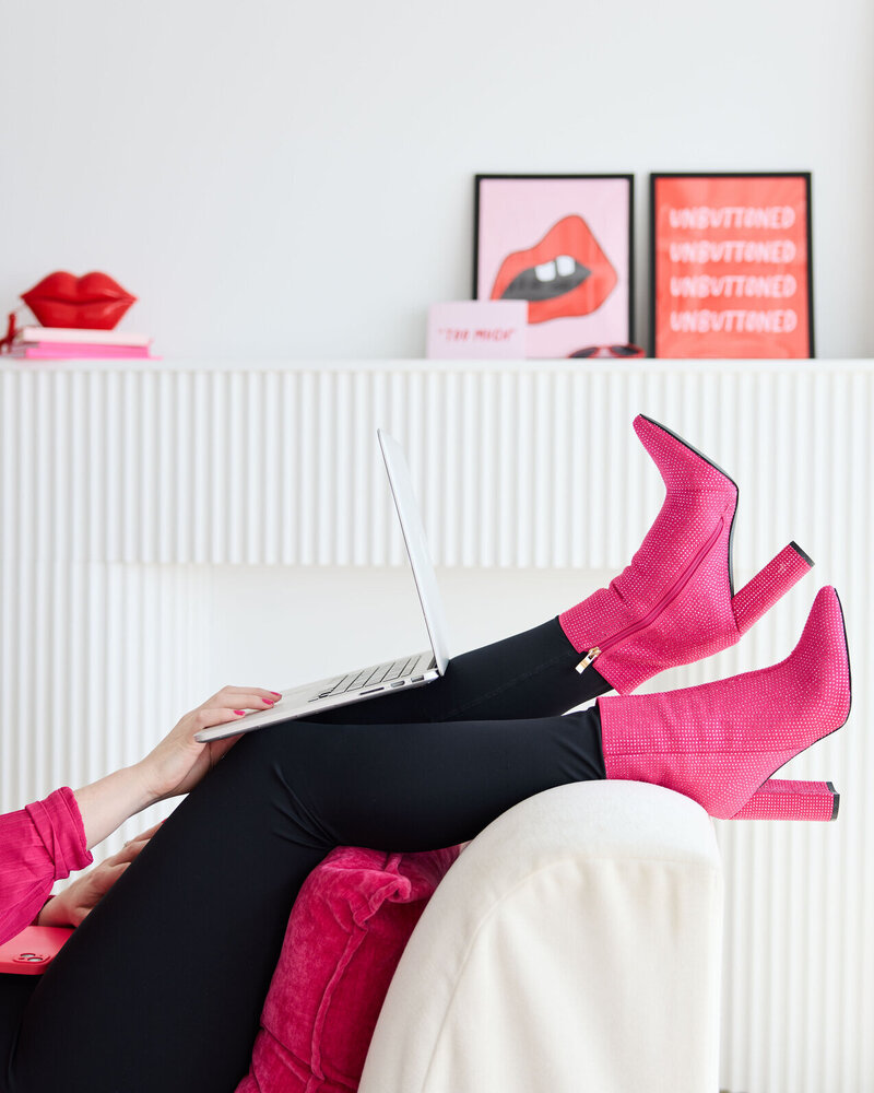 Emily, brand designer, holding laptop on her legs, wearing on-brand pink sparkly boots.
