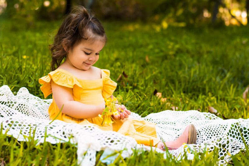 Little girl in yellow dress sitting in field of grass
