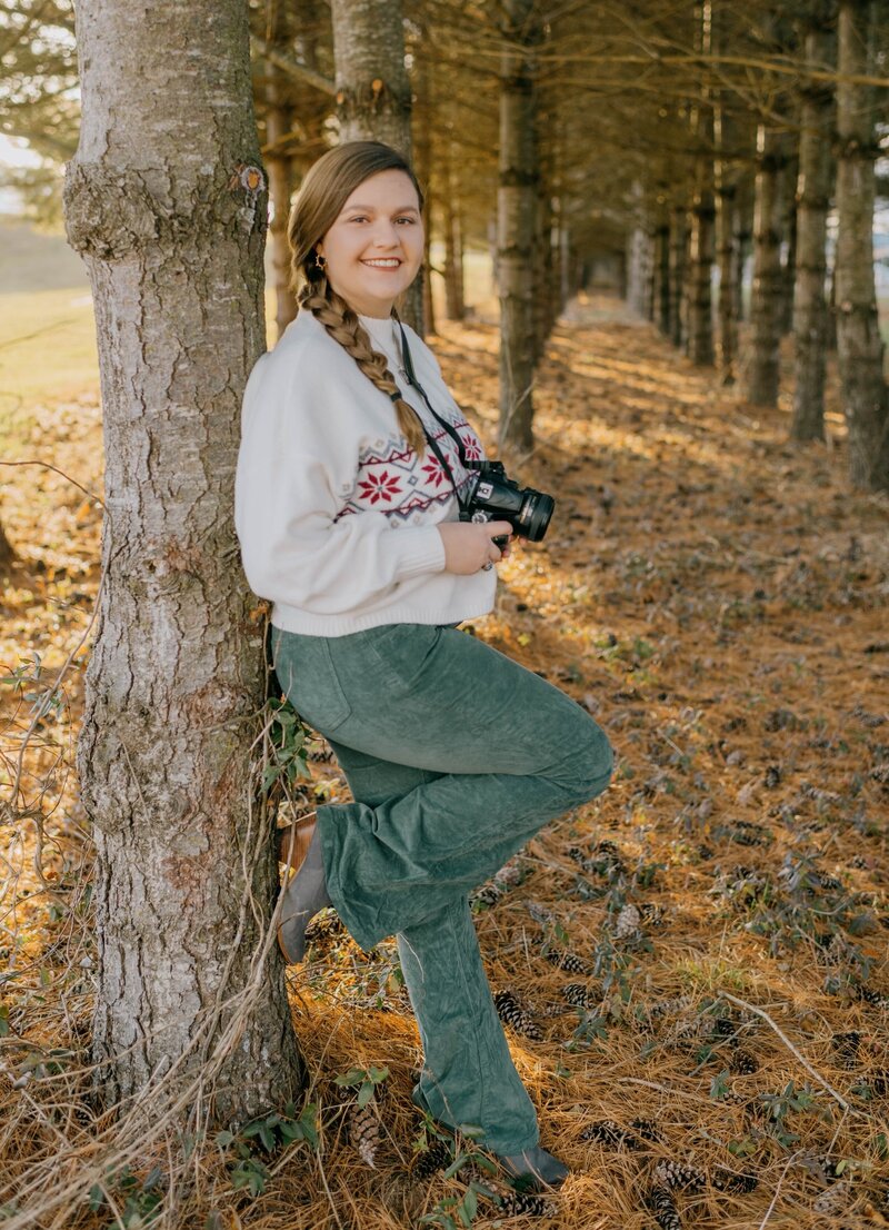 Sydney Coffman stands in the woods holding a Nikon camera.