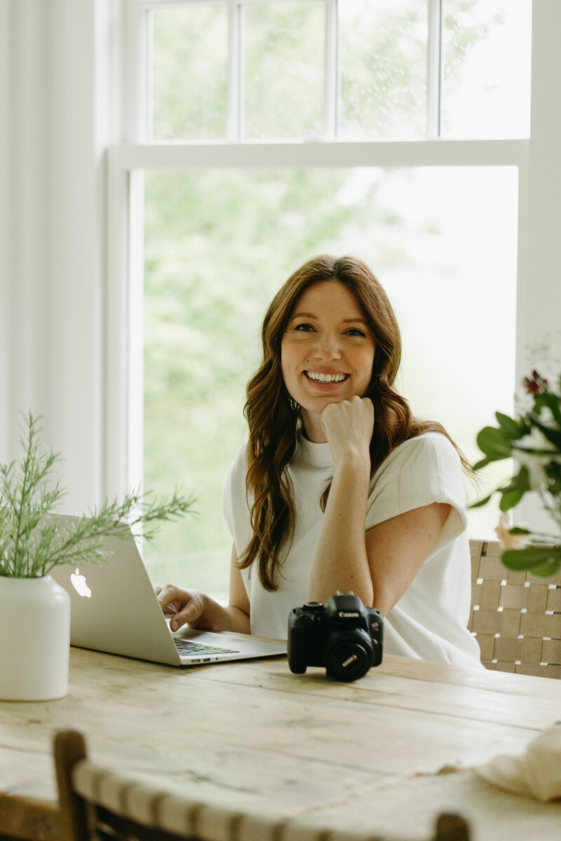 Marie-Catherine smiling while sitting at a desk with her laptop and camera