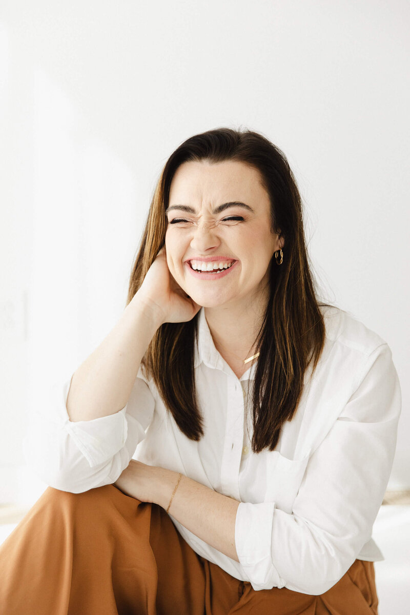 Brunette Woman in white shirt casually laughing with eyes shut