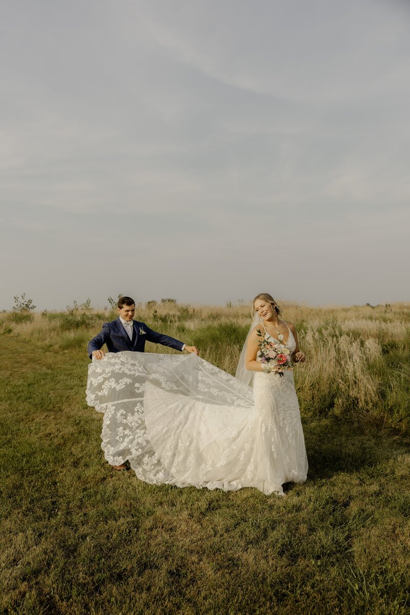 A groom proudly and tenderly spreads out the train of his new wife's wedding dress.